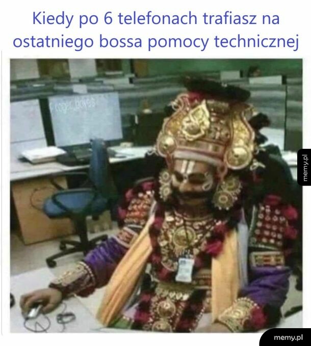 Osoba w tradycyjnym, bogatym stroju i makijażu siedzi przy biurku w biurze przed komputerem.