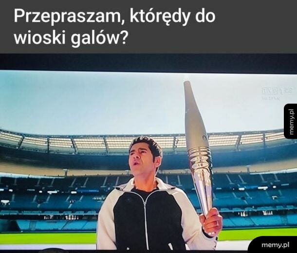 Mężczyzna z pochodnią olimpijską na stadionie z napisem u góry