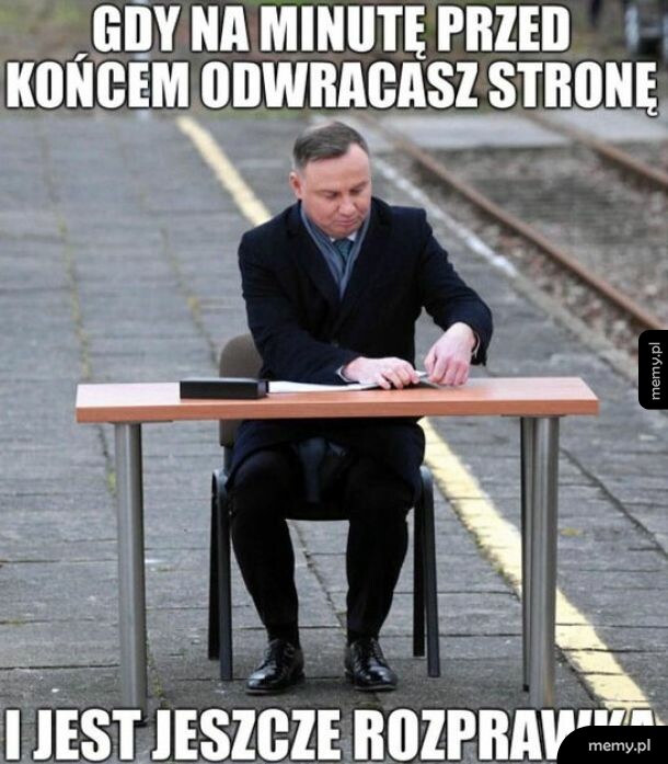 Andrzej Duda siedzi przy stoliku na peronie i przegląda dokumenty.