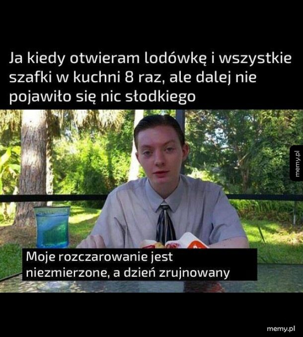 Mężczyzna w garniturze siedzi przy stole na zewnątrz, wyrażając rozczarowanie.